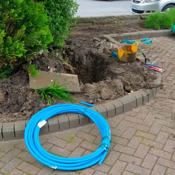 Burst mains water supply: excavation in a front garden with new blue MDPE pipe ready