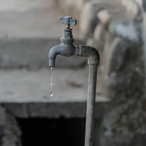 A close-up of a rustic outdoor faucet dripping water against a natural, textured background, symbolizing scarcity.