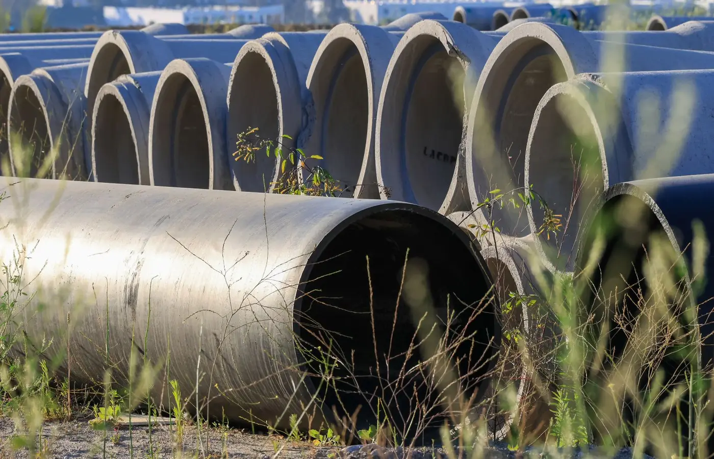 Stacked concrete pipes in an outdoor storage area surrounded by grass.