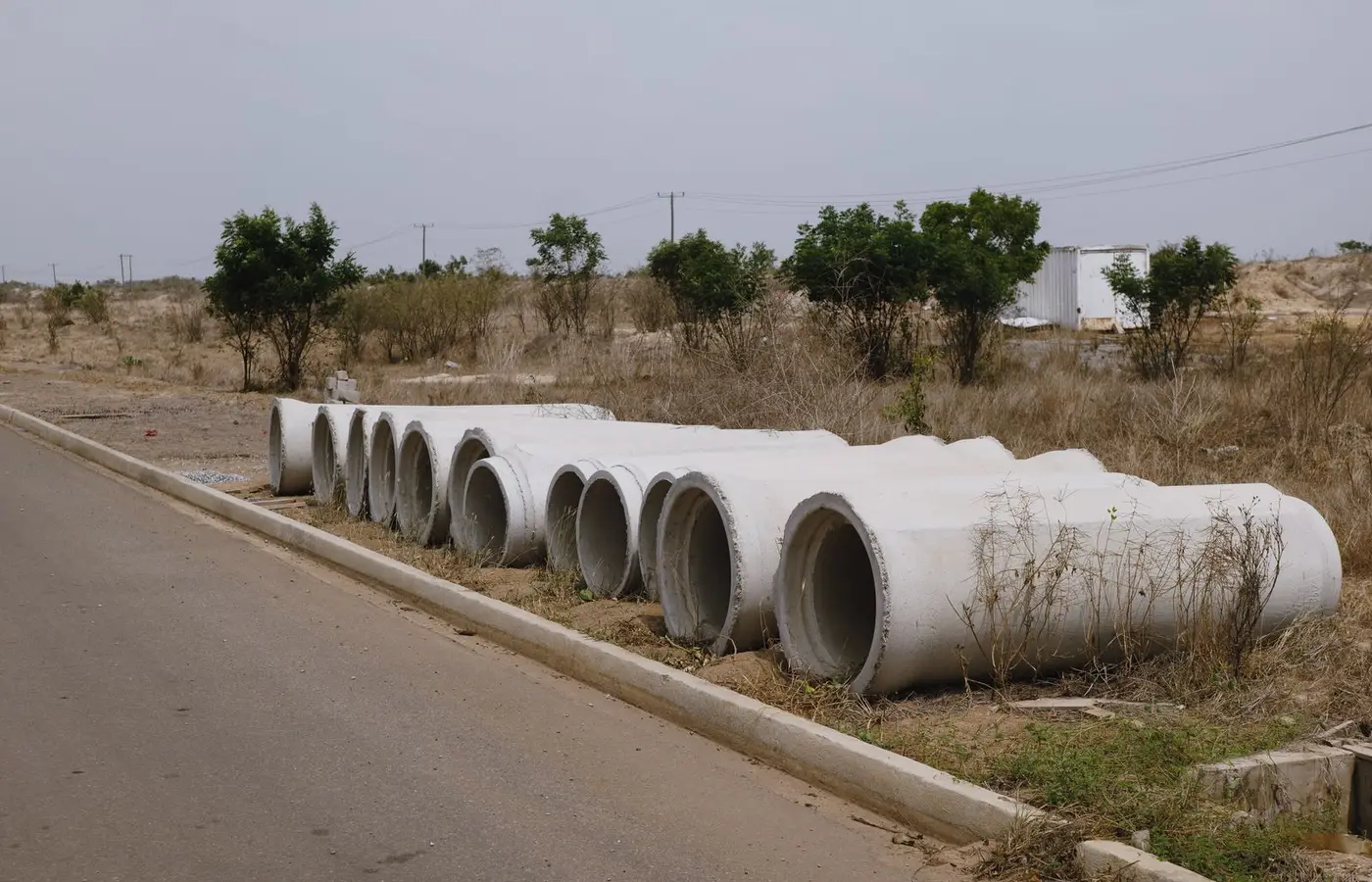 A row of concrete pipes on the roadside in a dry, rural setting.