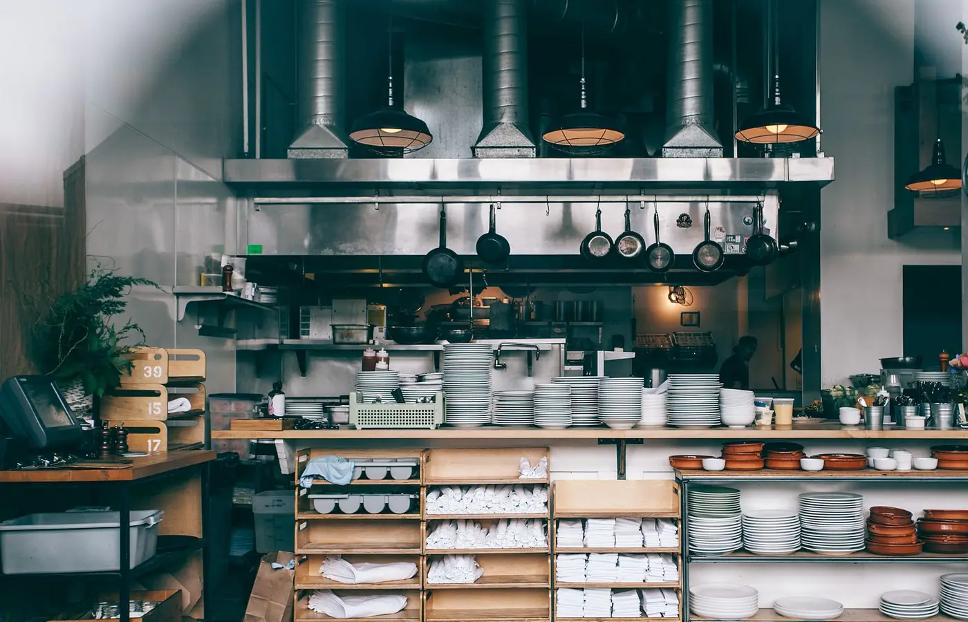 Spacious restaurant kitchen featuring stacked dishes, pans, and industrial lighting.