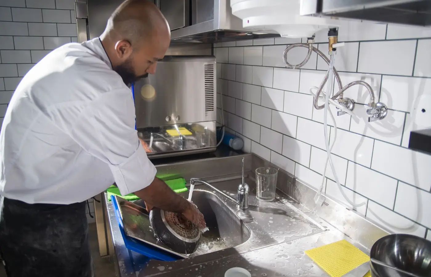 A chef cleans kitchen utensils in a stainless steel sink, maintaining hygiene standards.
