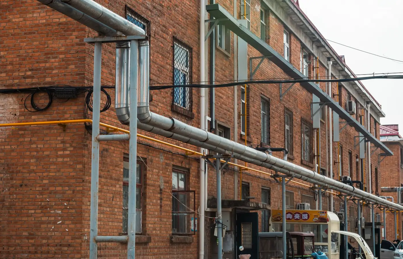 Exterior view of brick building with exposed industrial pipes and utility lines.