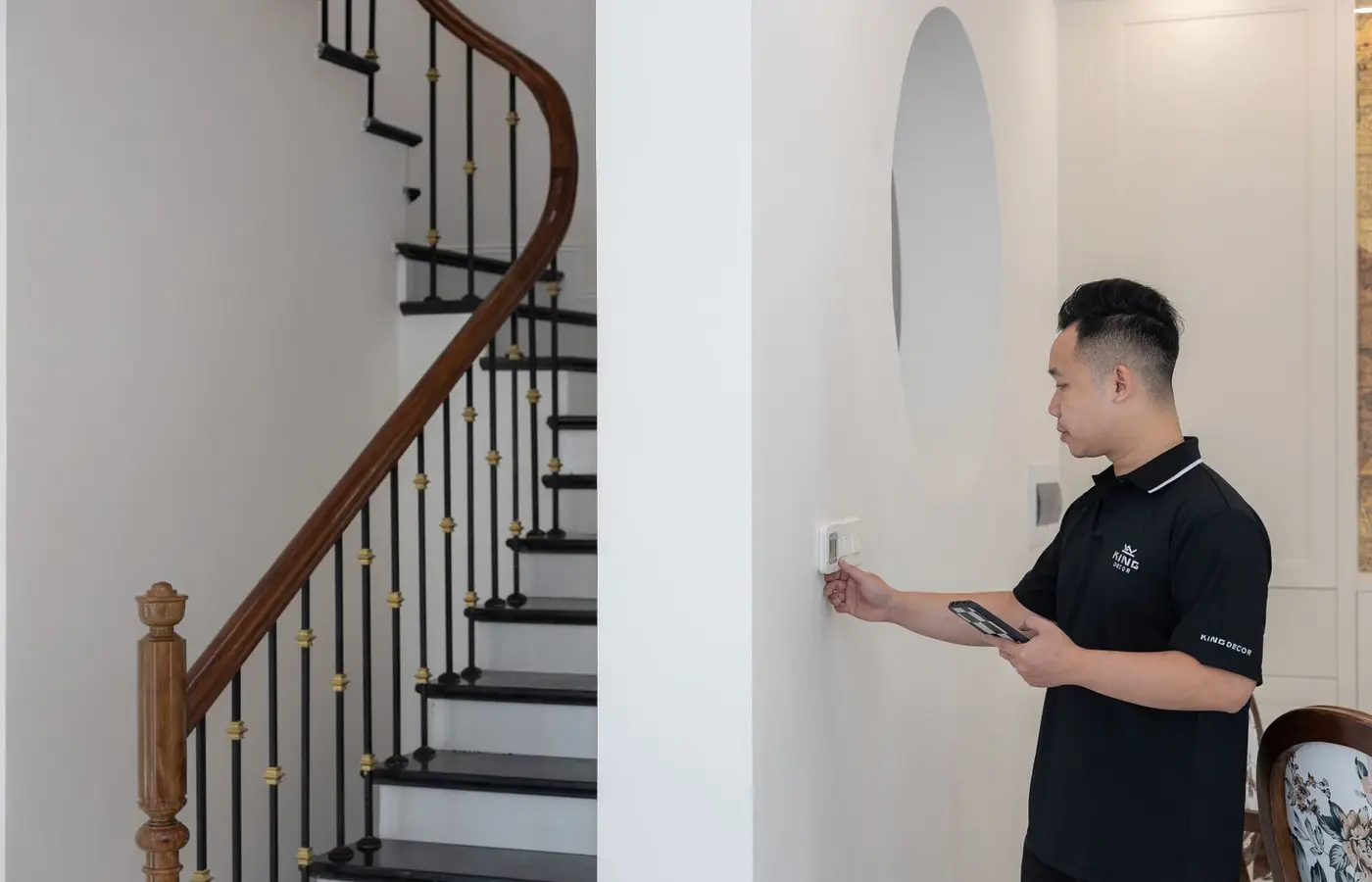 Man adjusting thermostat in stylish home with elegant staircase.