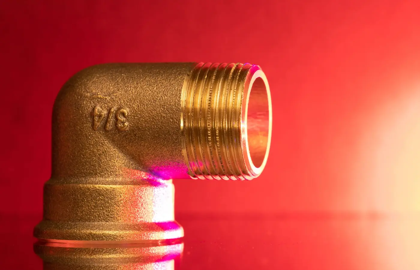 Close-up of a shiny brass pipe elbow fitting against a vibrant red backdrop, showcasing industrial elegance.