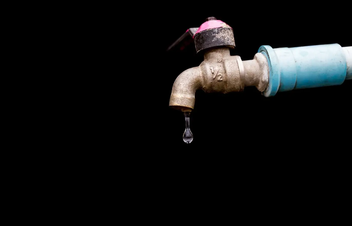 A detailed view of a metal faucet with a single water drop against a black background.