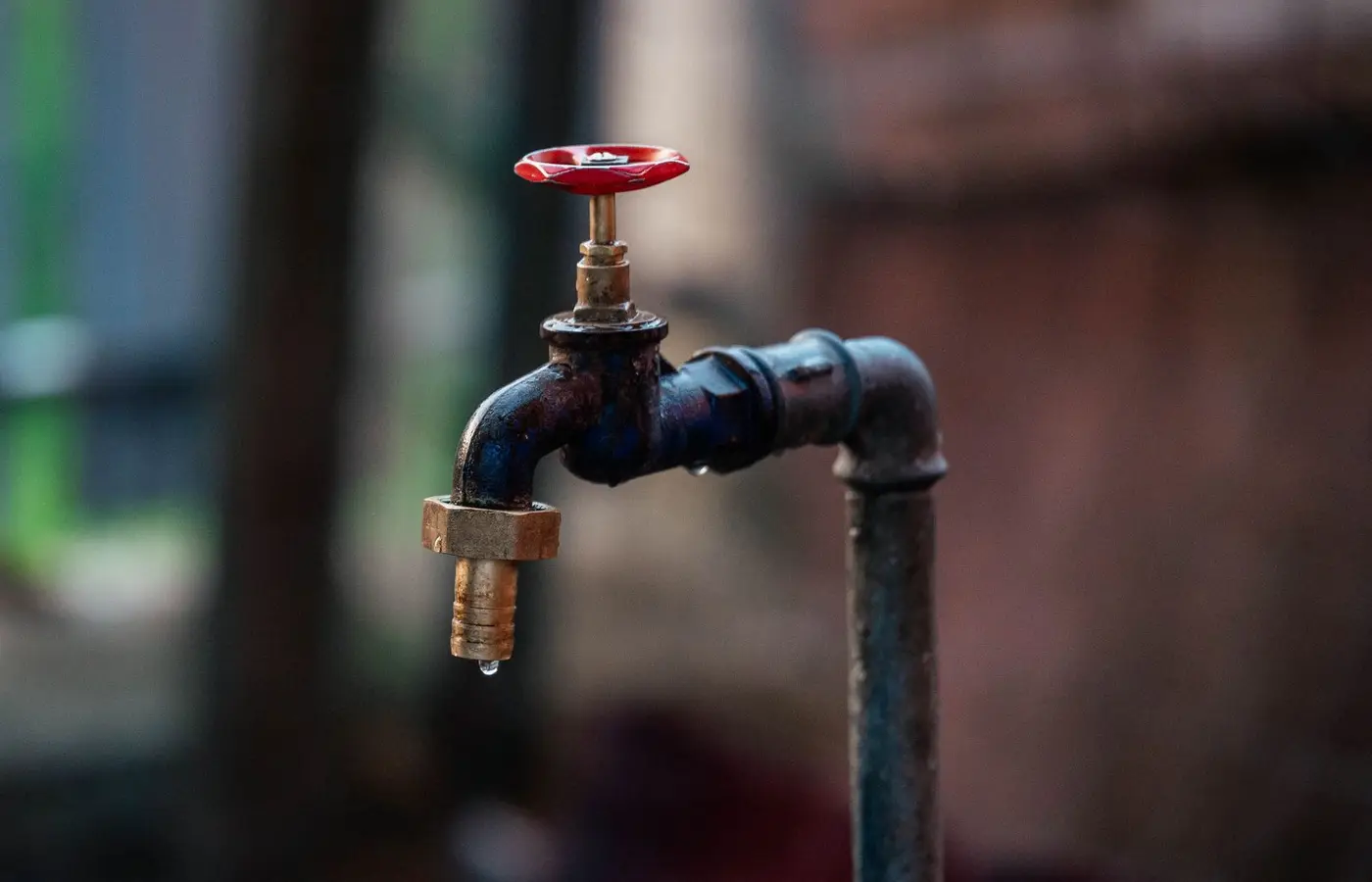 Close-up of a rusty outdoor water faucet with a single droplet falling from the spout.