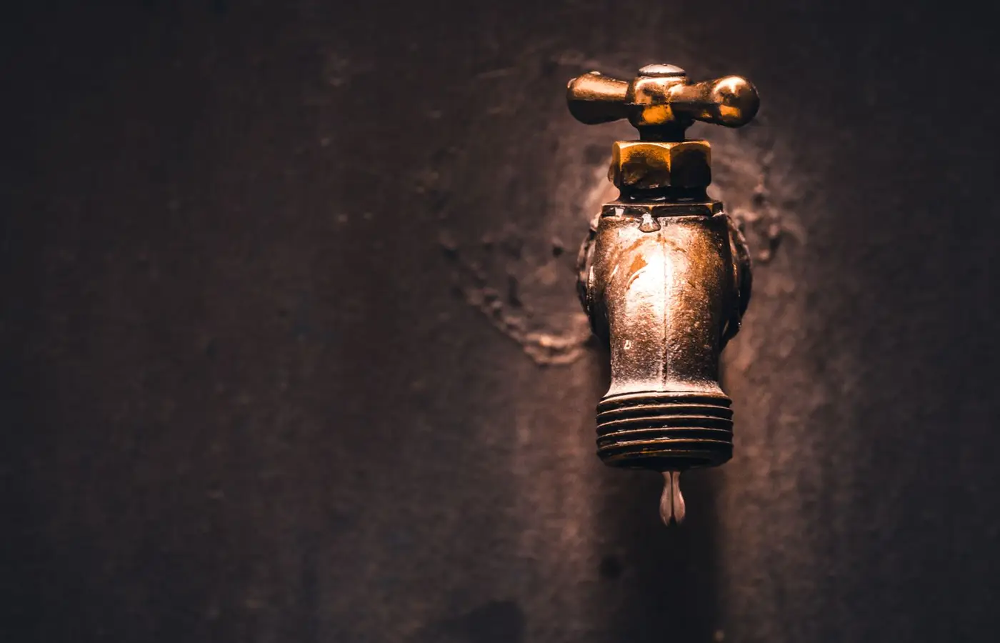 A close-up view of a vintage brass faucet with a single water droplet against a dark background.