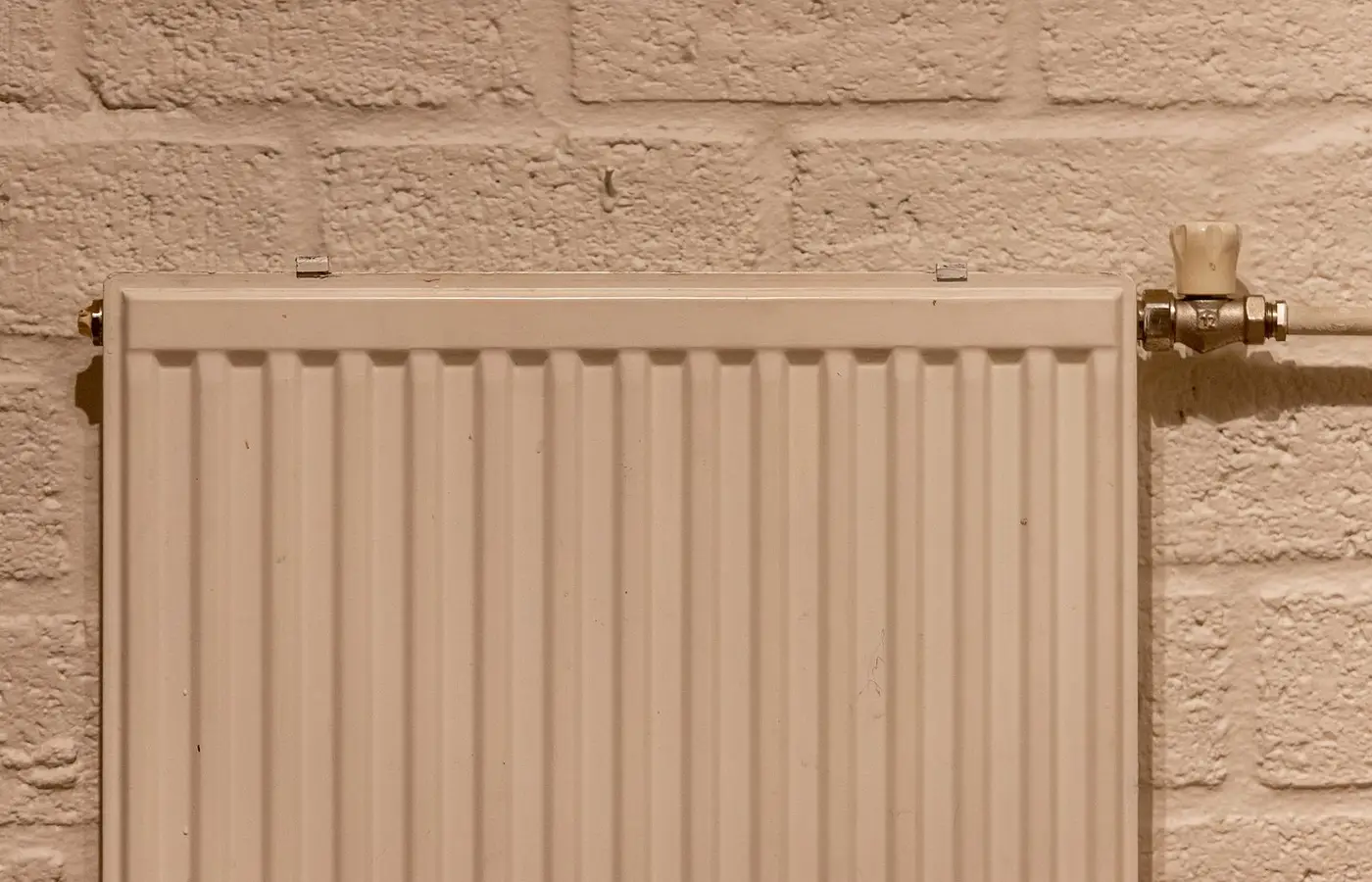 A clean white radiator mounted on a textured brick wall, indoors and well-lit.