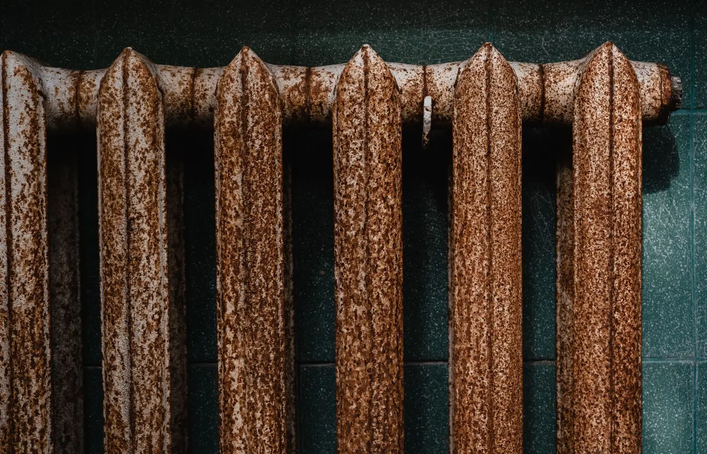 Close-up of a rusty old radiator with textured surface against green tiles, revealing industrial decay.