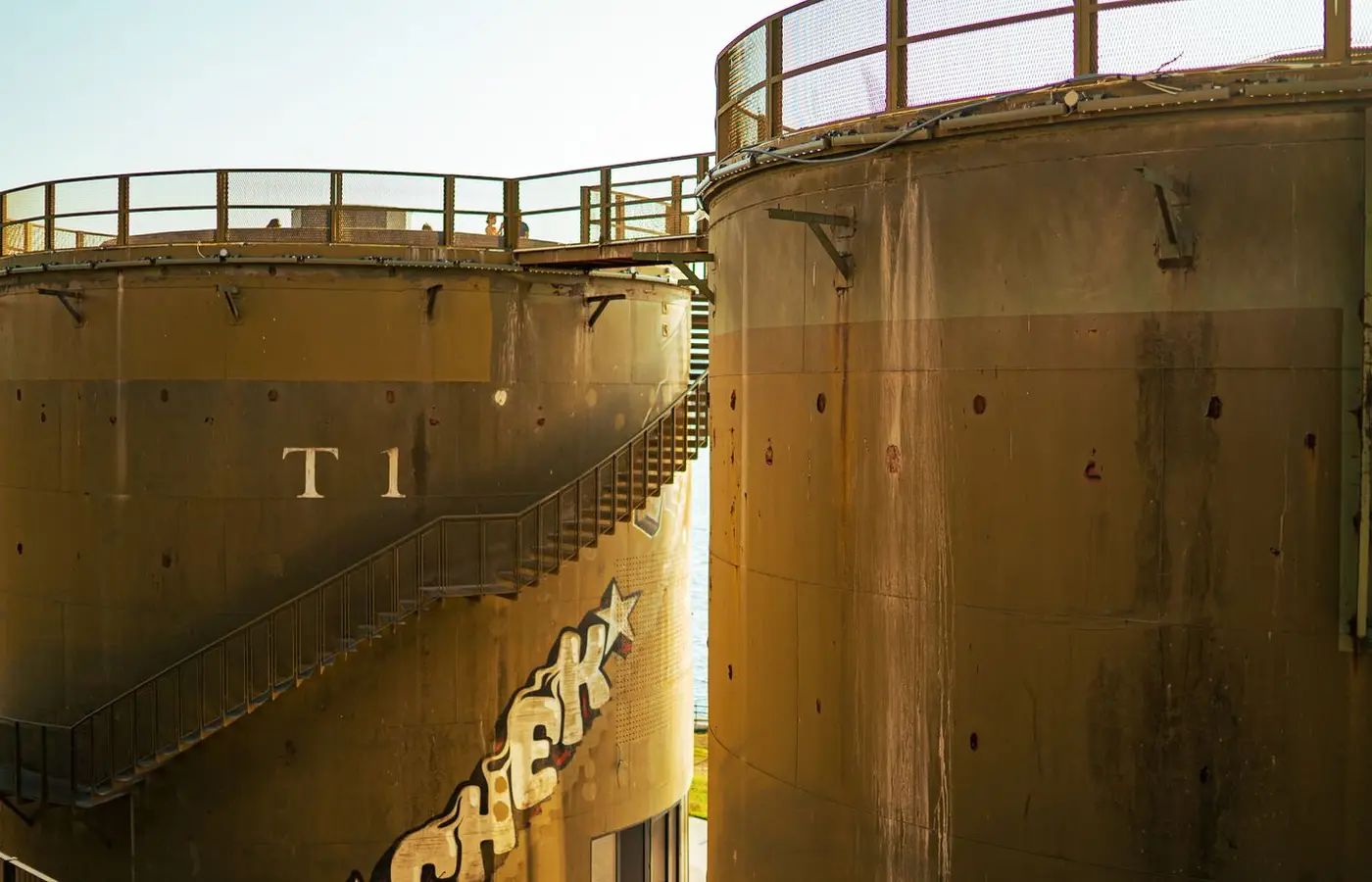 Close-up view of large industrial storage tanks with graffiti under sunny skies.