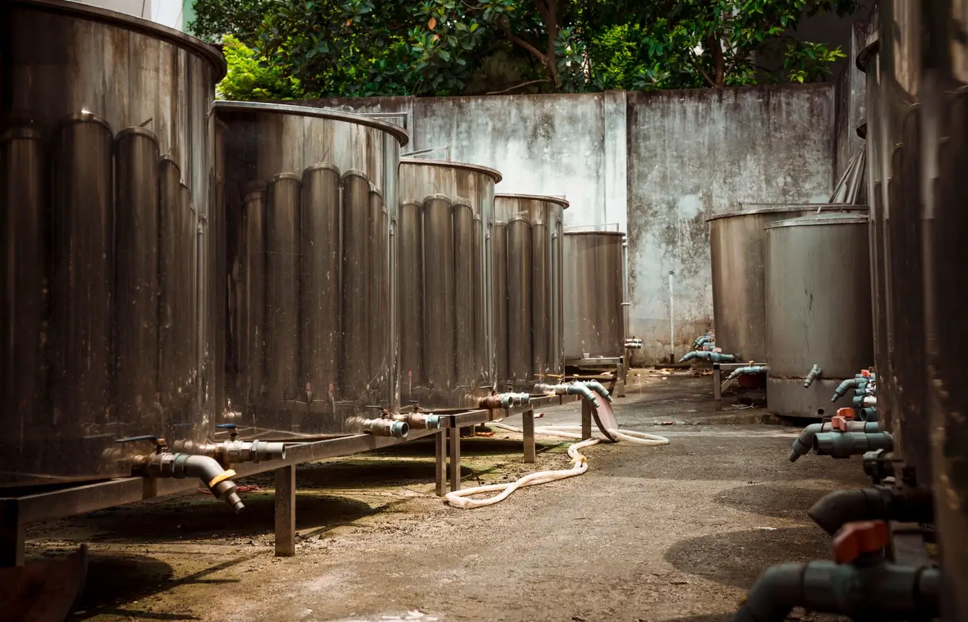 Outdoor view of large industrial metal tanks with connected pipes and concrete surroundings.