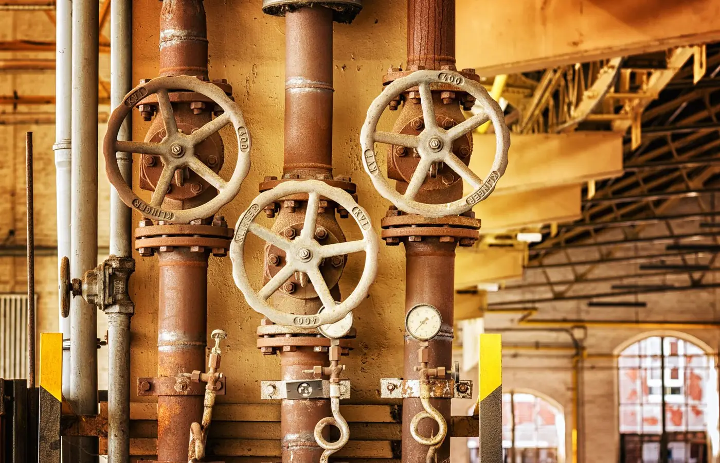 Close-up of rusty industrial pipes and valves, showcasing aging machinery in a factory setting.